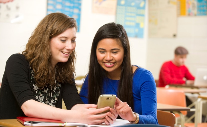 2 high school students looking at a smartphone in a classroom