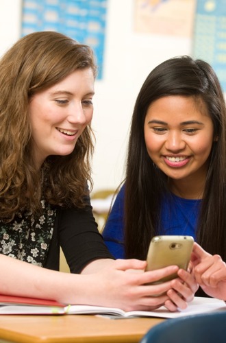 2 high school students looking at a smartphone in a classroom