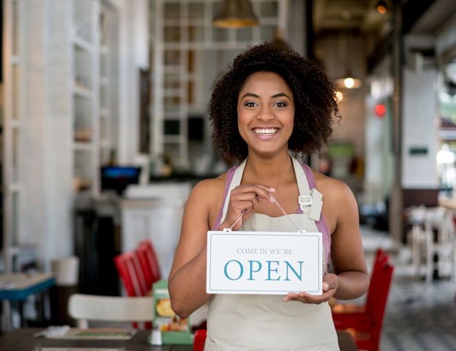 Person wearing an apron in a cafe holding an "open" sign