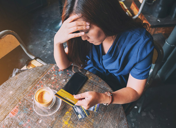Person having a coffee with head in hand unhappily holding a credit card