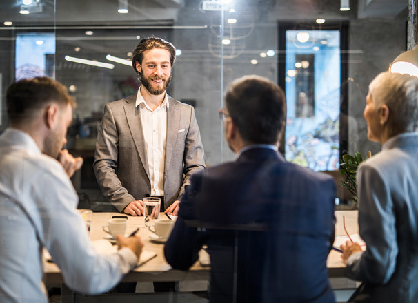 Person in a boardroom standing in front of 3 others during a meeting