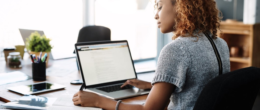 Person writing in a notebook with a laptop open on the desk