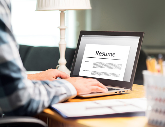 Hands typing on a laptop with the screen showing a resume