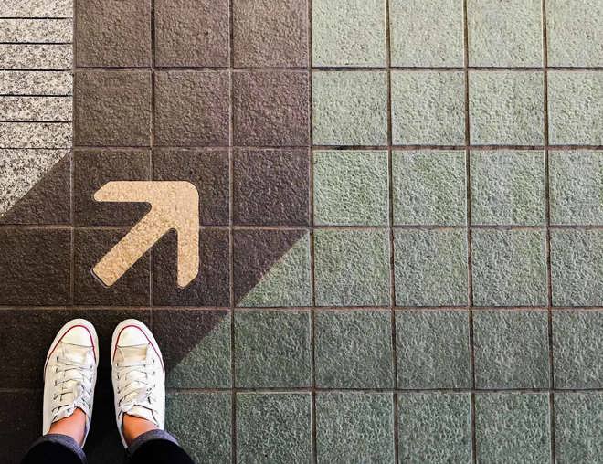 Overhead view of shoes standing on a sidewalk next to an arrow on the painted path