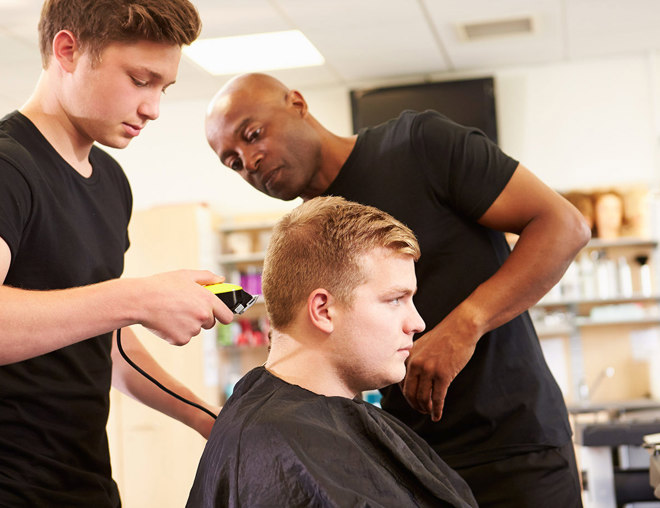 Hairdressing teacher instructs on a student on how to cut a person's hair.