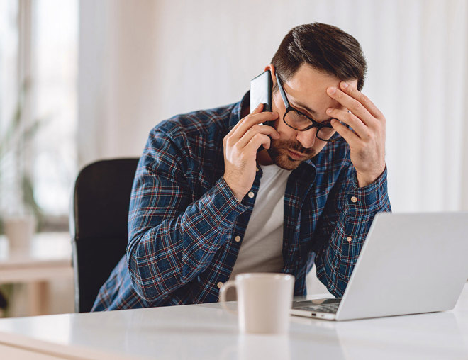 Worried man talking on phone while using laptop.