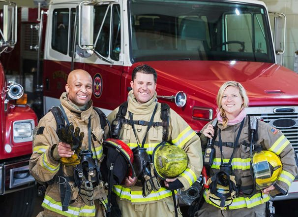 Diverse group of firefighters standing beside a firetruck.