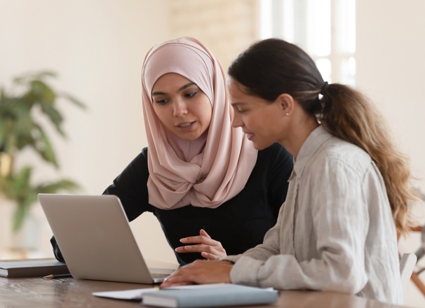 An employee training an intern on a laptop while they sit at an office desk. 