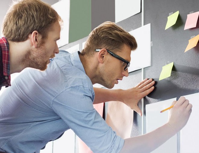 2 people writing on pieces of paper stuck  to the wall