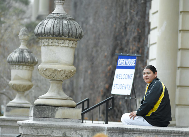 Student sitting outside a school building with an "Open House: Welcome Students" sign in the background