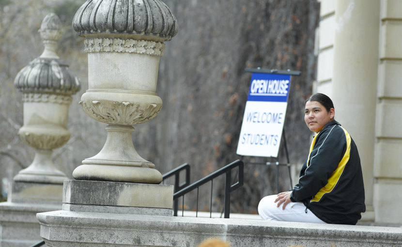 Student sitting outside a school building with an "Open House: Welcome Students" sign in the background