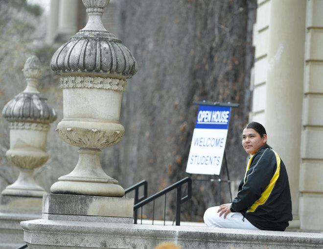 Student sitting outside a school building with an "Open House: Welcome Students" sign in the background
