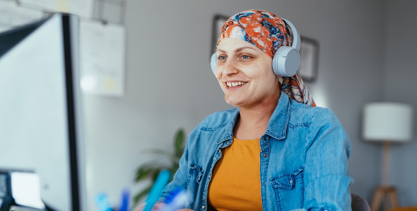 Person recovering from cancer sitting at desk and using a computer while listening to headphones.