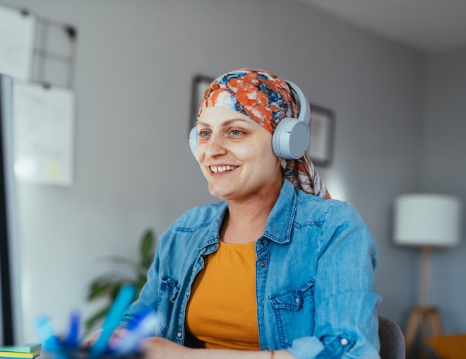 Person recovering from cancer sitting at desk and using a computer while listening to headphones.