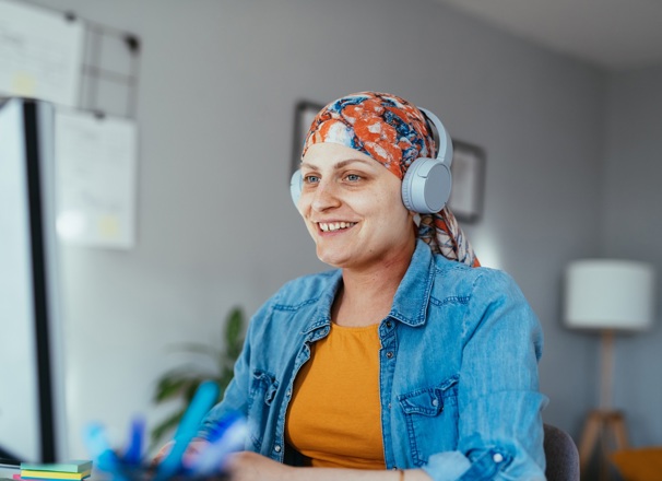 Person recovering from cancer sitting at desk and using a computer while listening to headphones.