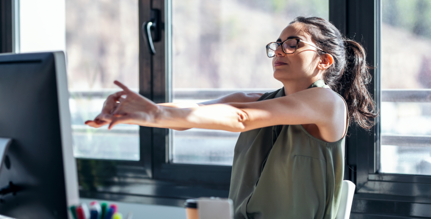 Office worker leaning back from computer and stretching arms.