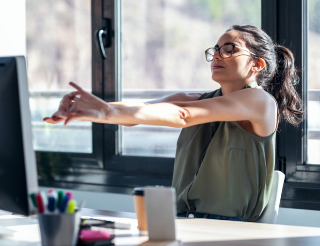 Office worker leaning back from computer and stretching arms.