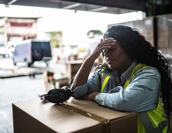 Tired warehouse worker leaning on a box.