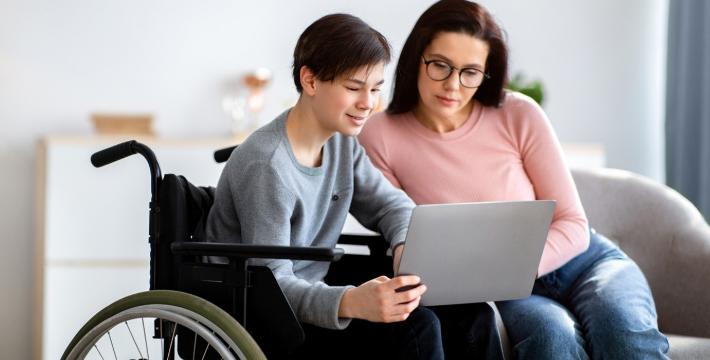 Parent assisting disabled teen on a laptop.