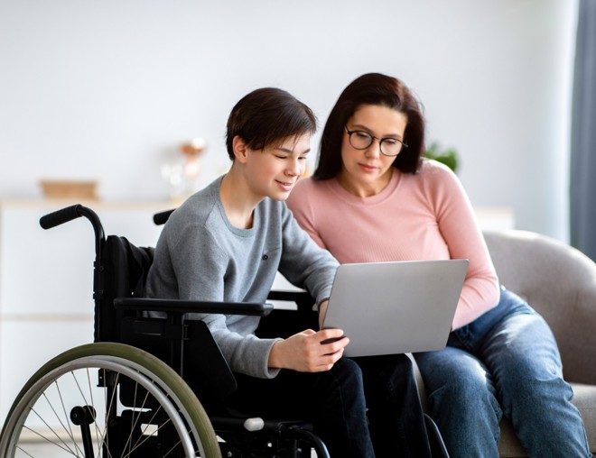 Parent assisting disabled teen on a laptop.