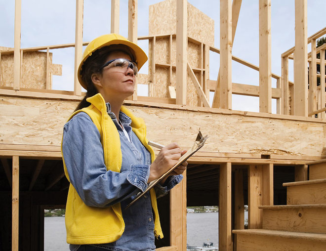 Person wearing a hard hat and safety glasses writing on a clipboard in a construction zone