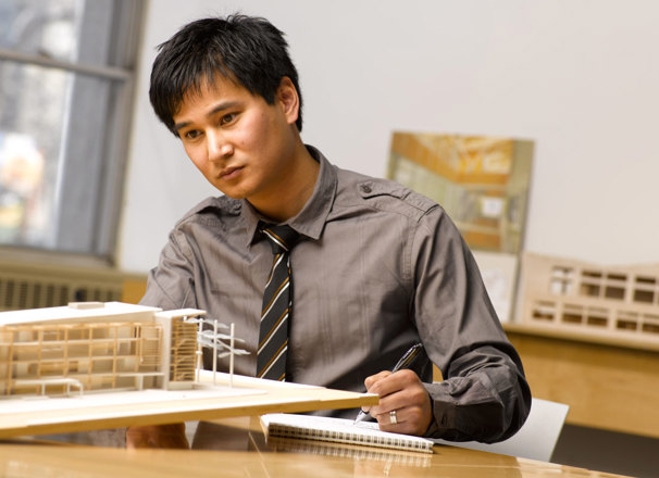 Architect in an office looking at a wooden model of a building