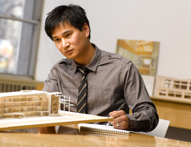 Architect in an office looking at a wooden model of a building