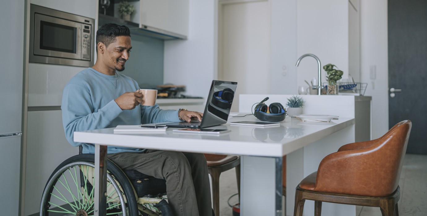 Person in wheelchair using their laptop at their kitchen table. 