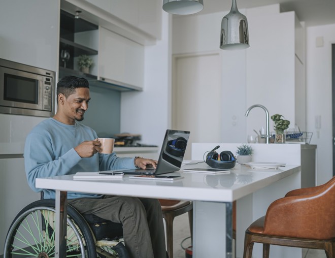 Person in wheelchair using their laptop at their kitchen table. 