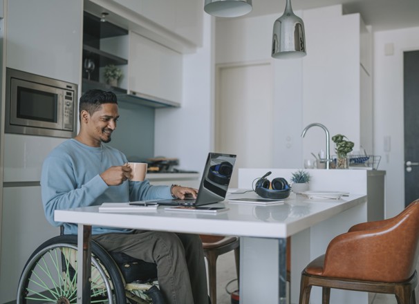 Person in wheelchair using their laptop at their kitchen table.