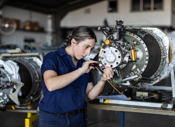 Apprentice aircraft engineer inspects parts in factory.