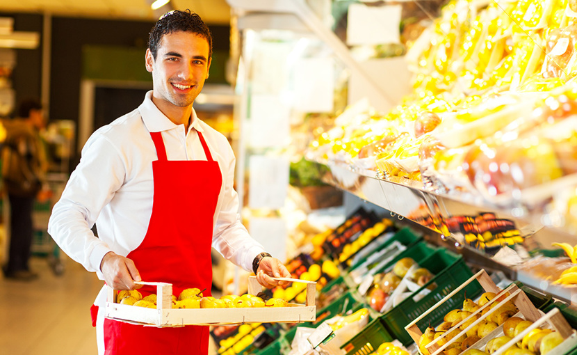Grocery store worker carrying fruit on a tray in the produce section