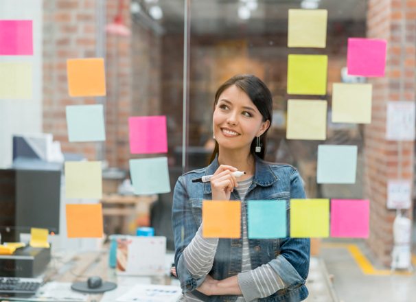 Person in front of a glass window full of sticky notes, holding a marker