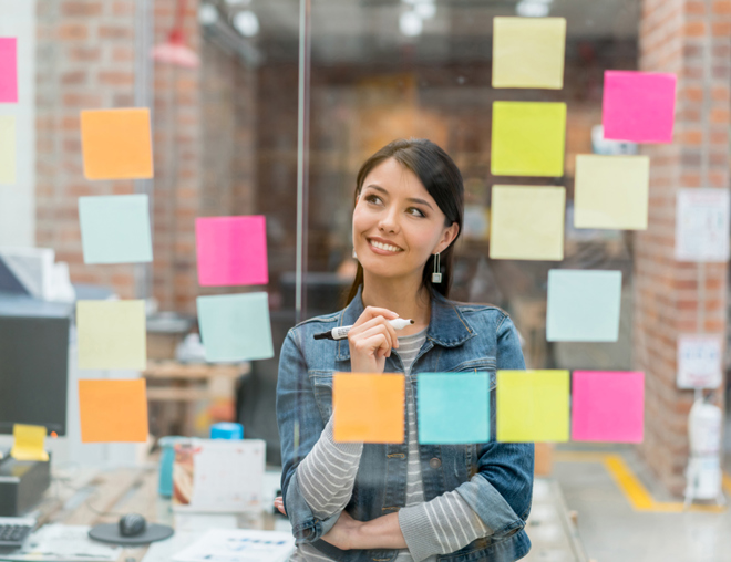 Person in front of a glass window full of sticky notes, holding a marker