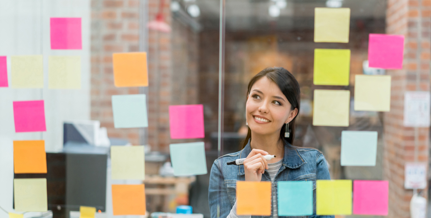 Person in front of a glass window full of sticky notes, holding a marker