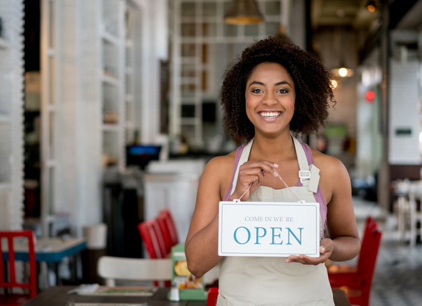 Person wearing an apron in a cafe holding an "open" sign