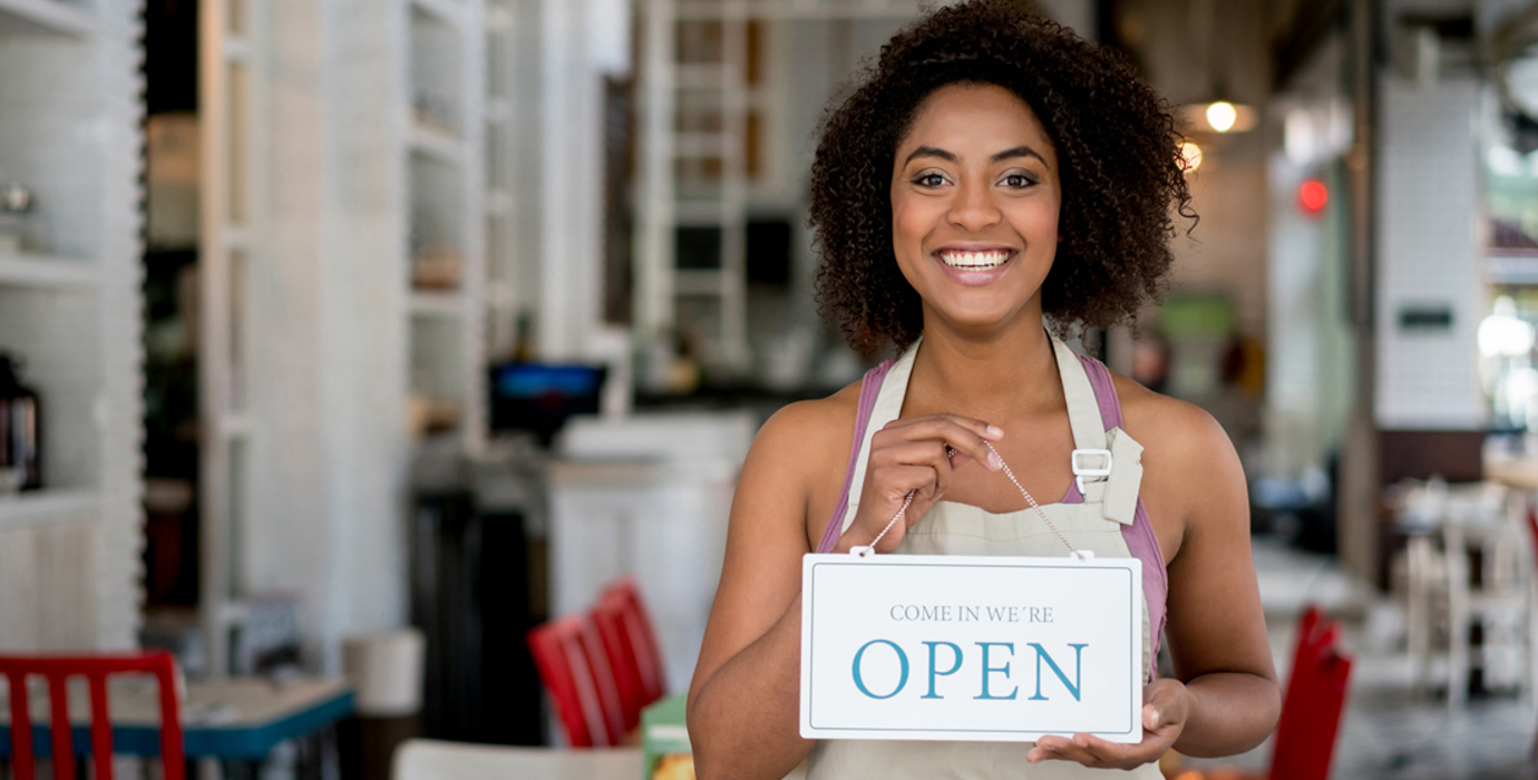 Person wearing an apron in a cafe holding an "open" sign