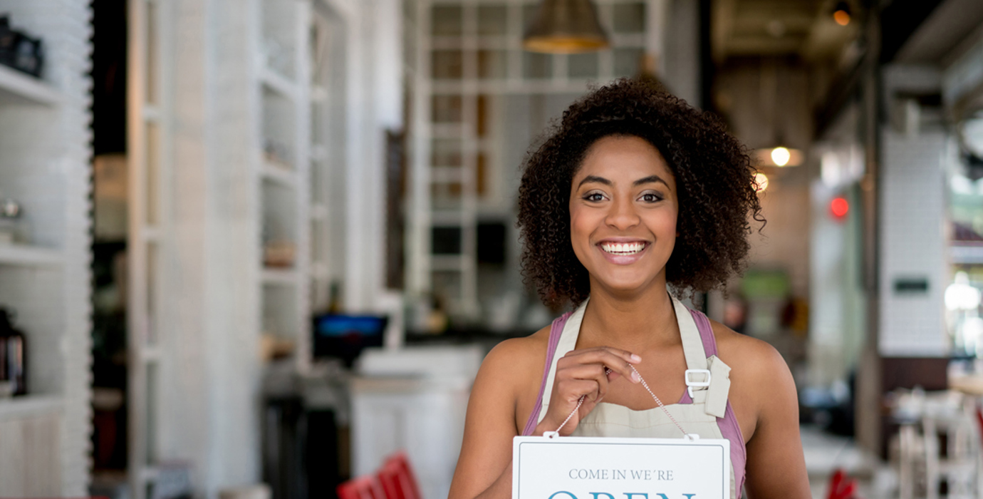 Person wearing an apron in a cafe holding an "open" sign