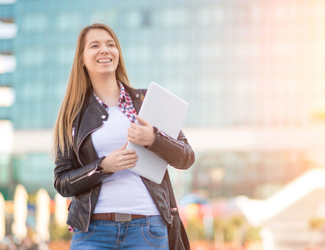 Person holding a laptop while standing outside in front of a glass building