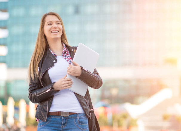 Person holding a laptop while standing outside in front of a glass building