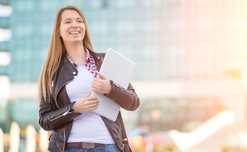 Person holding a laptop while standing outside in front of a glass building