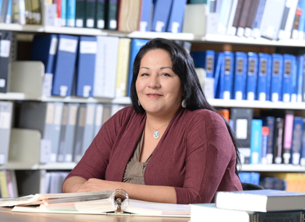 Person in a library sitting at a desk in front of bookshelves