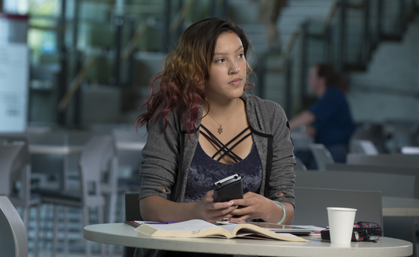 Youth thinking while holding a phone and sitting alone at a table