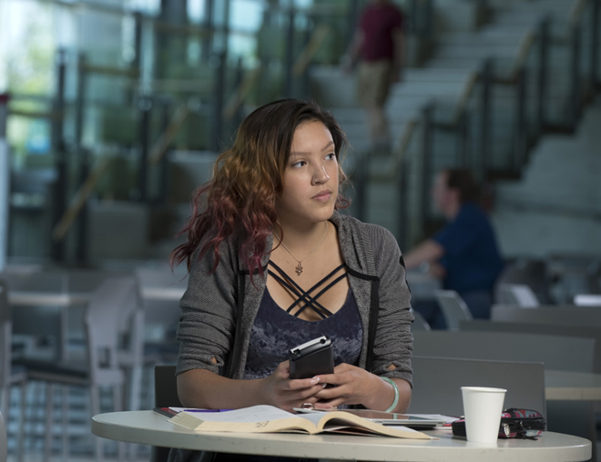 Youth thinking while holding a phone and sitting alone at a table