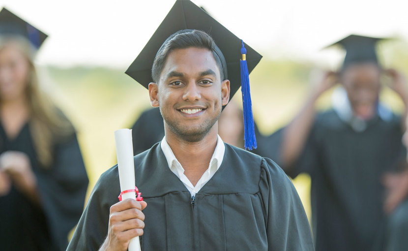 Graduate wearing cap and gown holding up a diploma