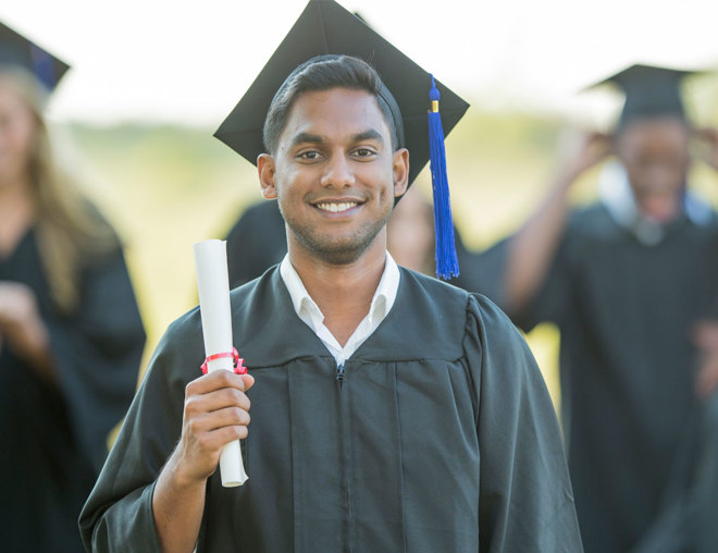 Graduate wearing cap and gown holding up a diploma