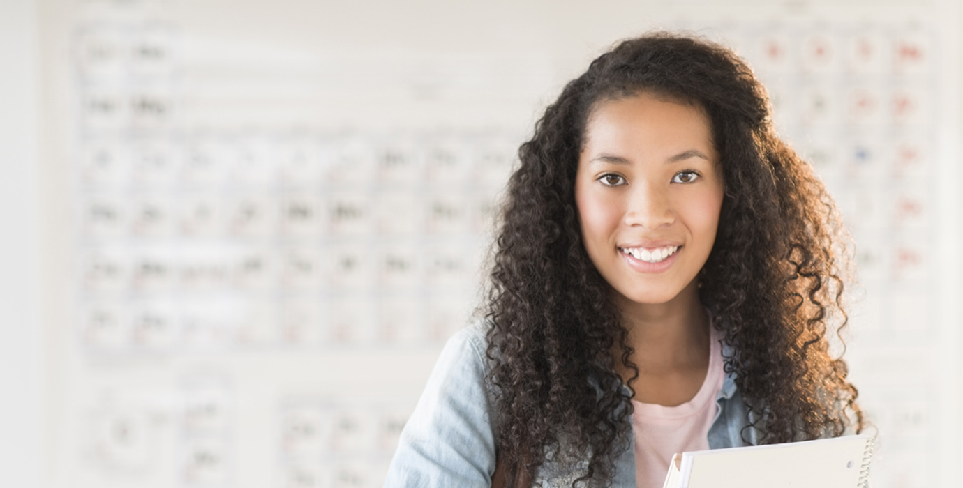 Youth smiling and standing in front of a periodic table