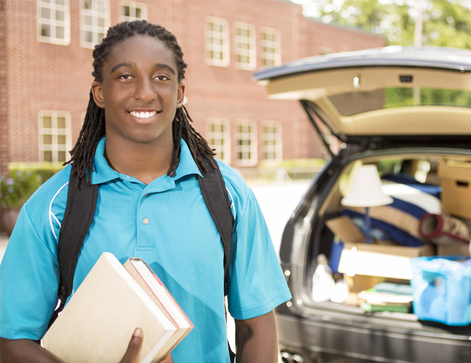 Youth standing behind a vehicle with an open trunk full of things