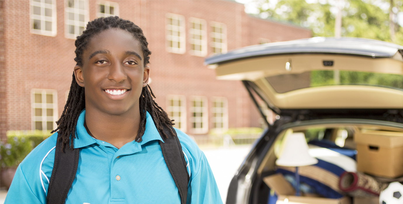 Youth standing behind a vehicle with an open trunk full of things