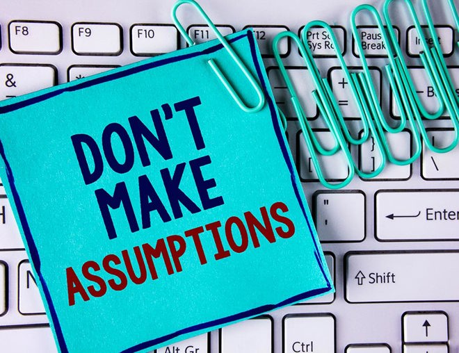 Note saying "don't make assumptions" and paper clips on a keyboard